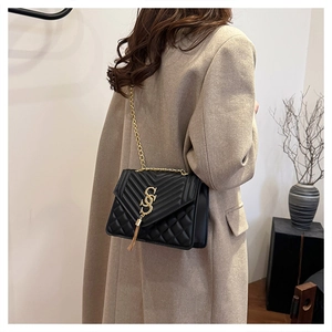 Detail of black quilted shoulder bag with gold chain strap on a beige cashmere coat