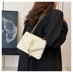 White quilted crossbody bag with gold chain strap and tassel detail on a female model