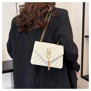 Detail of white quilted crossbody bag with gold chain and metal tassel on black blazer