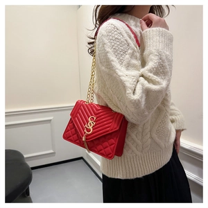 Detail of red quilted shoulder bag with gold chain strap and decorative tassel