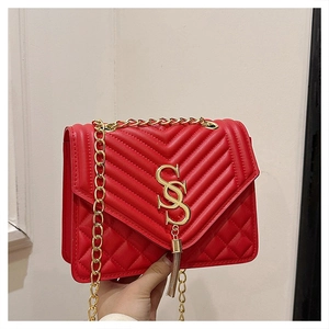 Close-up of red quilted faux leather bag with gold S-logo and fringe tassel detail