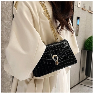 Detail of black crocodile pattern shoulder bag with gold chain and metal buckle closure