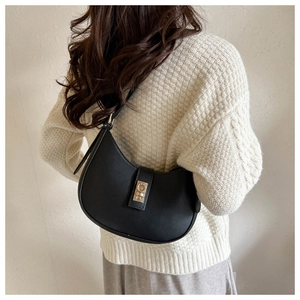 Sac hobo croissant noir minimaliste avec fermoir doré porté par un mannequin en pull blanc