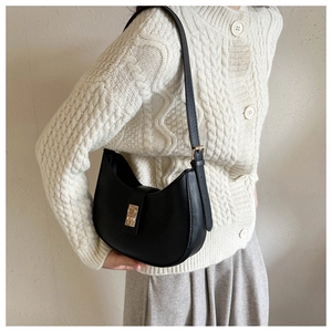 Détail du sac sous le bras noir en demi-lune avec boucle dorée sur gilet en maille