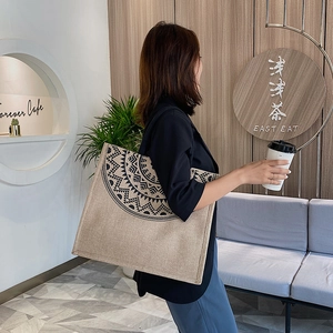 Lifestyle view of a large linen tote bag with black mandala pattern in a cafe setting