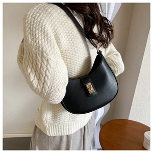 Détail d'un sac sous le bras en forme de croissant noir avec boucle dorée sur modèle