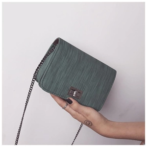 Detailed view of the dark green textured small square bag with a metal turn-lock and chain