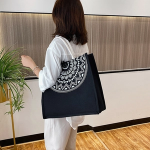 Large black canvas tote bag with white mandala pattern worn by a model in a modern home