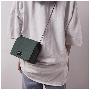 Detail shot of the dark green textured crossbody bag with metal chain strap on model