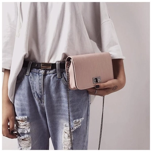 Close-up of pink litchi grain leather flap bag with silver turn-lock on casual outfit