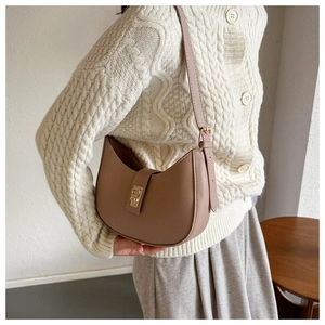 Sac demi-lune en cuir marron avec fermoir doré porté par mannequin en gilet