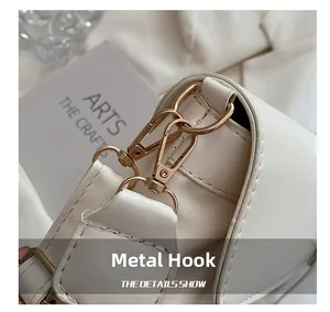 Close-up of premium light gold metal hook hardware on a white leather shoulder bag