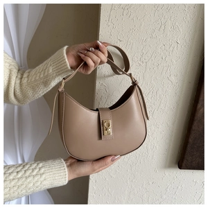 Détail du sac croissant camel avec fermoir doré sur un fond beige texturé