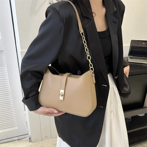 Khaki leather baguette bag with gold chain strap and twist lock on a shoulder