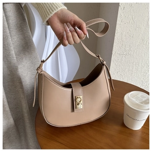 Détail du sac croissant en similicuir beige avec fermoir doré posé sur une table en bois