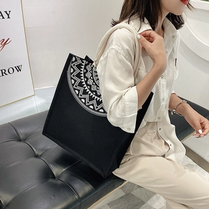 Detail of black canvas tote bag with white geometric folk pattern and rope handles
