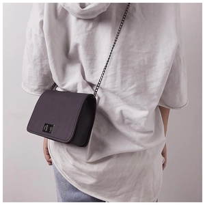 Detail view of black textured crossbody bag with silver rotating lock and chain strap