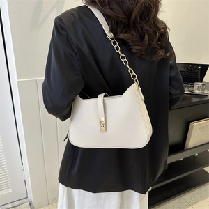 Minimalist beige leather shoulder bag with gold clasp shown on model in modern interior