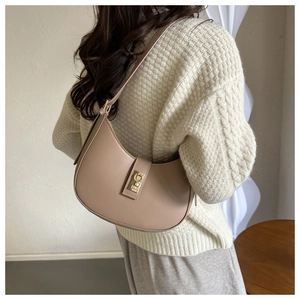 Gros plan d'un sac demi-lune beige en cuir lisse avec boucle métallique porté par le modèle