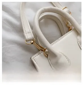 Detail of reinforced golden metal hooks and round handle on a cream leather crossbody bag