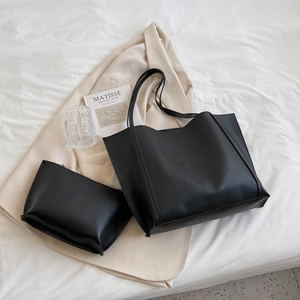 Minimalist black faux leather tote bag set with matching inner pouch on a bed