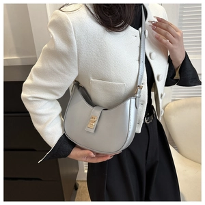 Détail du sac hobo argenté avec boucle dorée porté sur une veste en tweed blanc