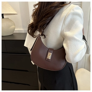 Détail du sac demi-lune en cuir marron foncé avec boucle dorée porté à l'épaule