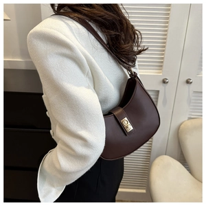 Détail d'un sac sous le bras en forme de croissant marron foncé avec boucle dorée mate