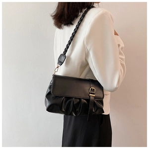 Detail of black pleated shoulder bag with gold buckle and woven strap on model