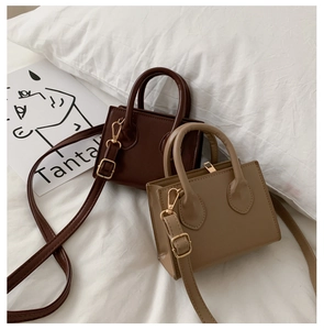 Detail view of dark coffee and beige mini crossbody bags with gold hardware on white bedding