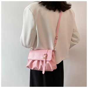 Detail of light pink pleated shoulder bag with gold buckle on white blazer background