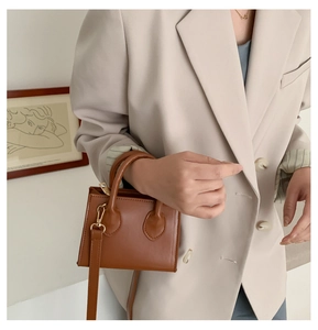Mini brown leather square bag with round handle and gold hardware shown on a model