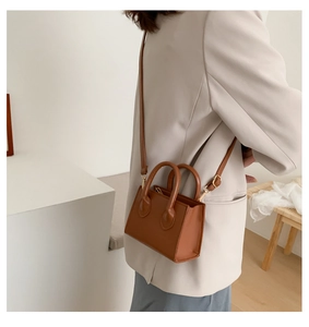 Brown mini crossbody bag with gold hardware shown on model in a minimalist setting