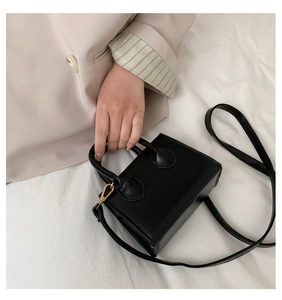 Detail of black faux leather crossbody bag with cylindrical handles and gold buckles