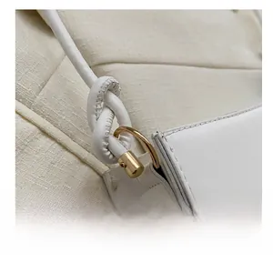 Macro detail of white leather shoulder bag featuring gold hardware and knotted strap
