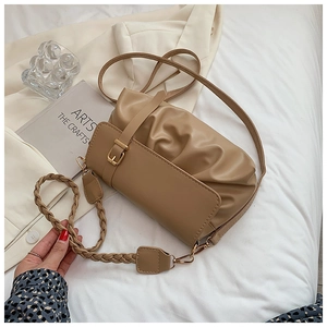 Detail of beige pleated cloud bag with braided strap and metal buckle on white fabric