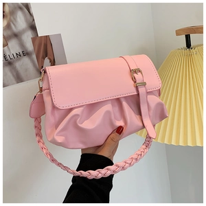 Pink faux leather shoulder bag with ruched design and woven handle on magazine background