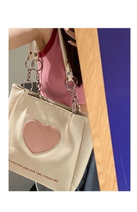 Detailed shot of white tote bag featuring pink heart patch and metal chain strap details