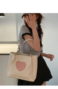 Detail of off-white tote bag with pink heart patch and silver metal ring handle
