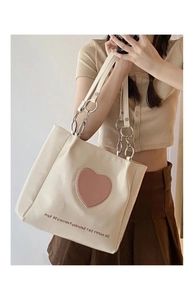 Detail of cream tote bag featuring a pink heart patch and stylish metal chain strap