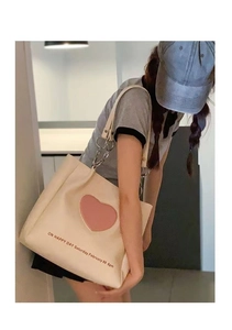 Off-white large capacity tote bag with pink heart patch shown on shoulder by model