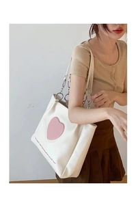 Detail of white tote bag featuring pink heart patch and silver metal ring hardware