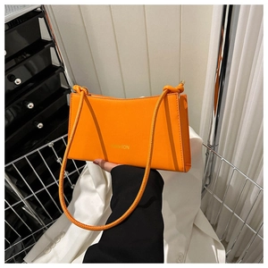 Detail of orange leather baguette bag with gold lettering and decorative knotted strap