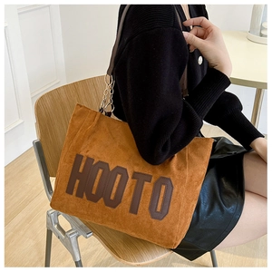 Detail of a brown suede tote bag featuring large HOOTO lettering and metal chain strap