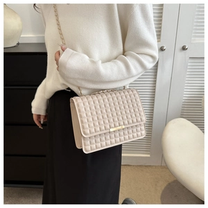 Dettaglio di una borsa a tracolla trapuntata beige con catena dorata e fibbia in metallo