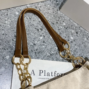 Detail of beige tote bag featuring stylish gold chain links and brown leather straps