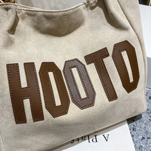 Detail of beige fleece tote bag featuring brown leather HOOTO appliqué and stitched letters