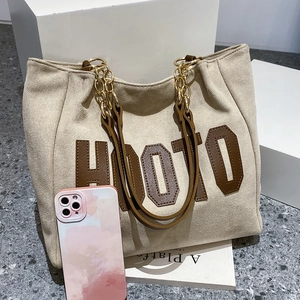 Detail of beige tote bag with HOOTO logo, plush suede texture and golden chain strap