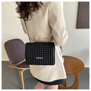 Dettaglio borsa a tracolla trapuntata nera con inserto dorato su blazer beige