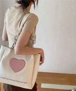 Creamy white tote bag with pink heart decor and silver metal rings shown on a model